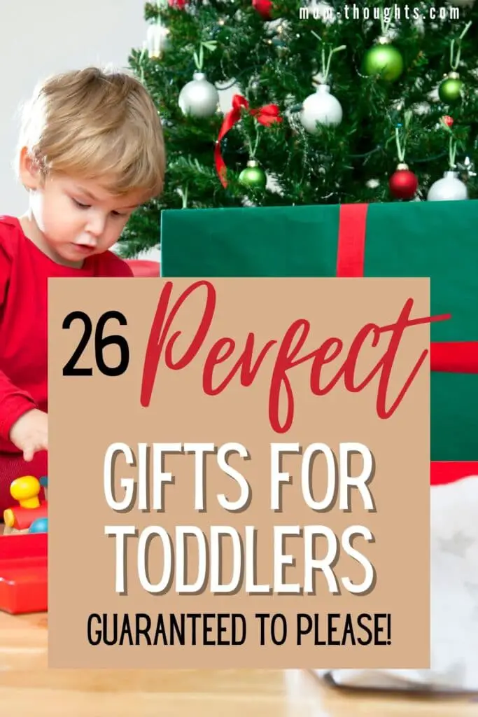 This image is of a toddler boy sitting in front of a Christmas Tree opening a present. There is text overlay that says "26 perfect gifts for toddlers guaranteed to please!"